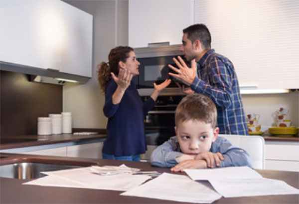 Мальчик сидит за столом. На заднем плане ругаются родители