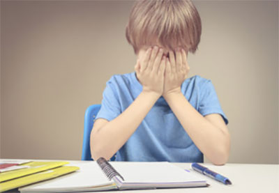 Расстроенный мальчик с закрытым лицом, рядом лежит открытая тетрадь