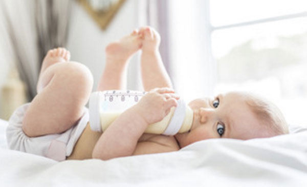 Грудной ребенок пьет из бутылочки. Он улыбается