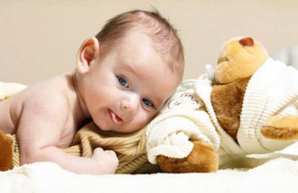 Грудничок лежит на животике, под ним плюшевый медведь
