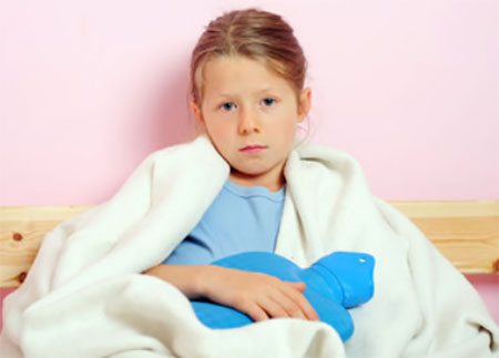 Замерзшая девочка укуталась в одеяло, держит грелку