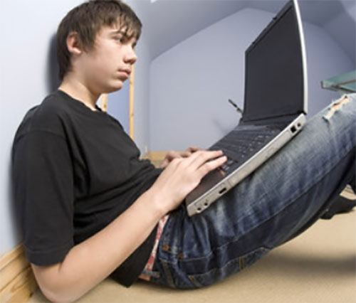 Тринадцатилетний мальчик сидит на полу и играет на ноутбуке