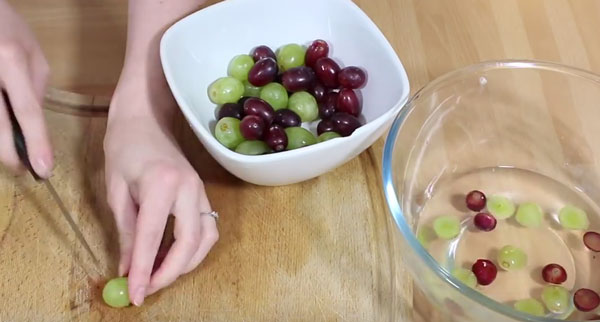 В одной емкости вымытый виноград, в другой нарезанный, который плавает в сиропе. На досточке продолжают нарезать