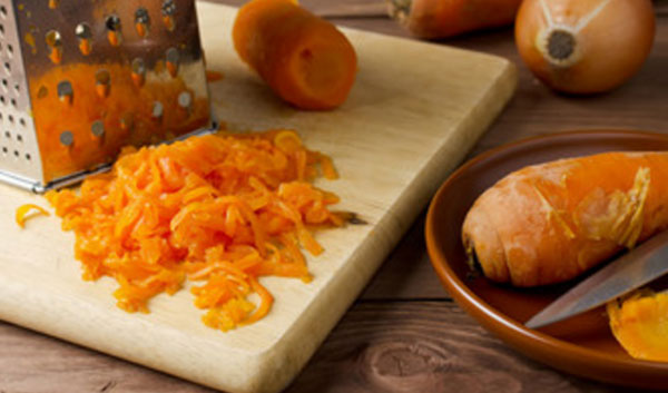 Отварная морковь, частично натертая на терке, терка и миска с неочищенными овощами