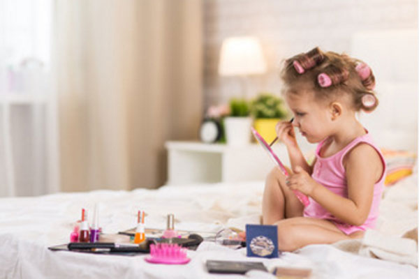 Девочка сидит на кровати. Наносит себе детскую косметику