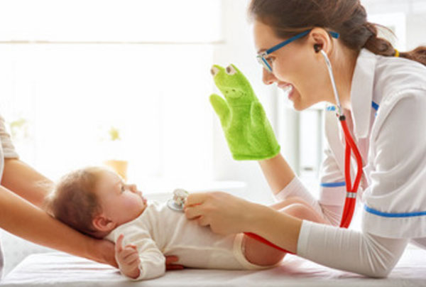 Доктор отвлекает грудного ребенка игрушкой. Слушает его грудку