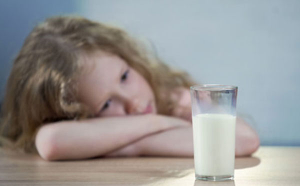 Грустная девочка смотрит на стакан с молоком