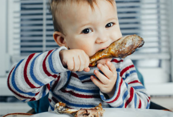 Маленький ребенок ест запеченную куриную голень