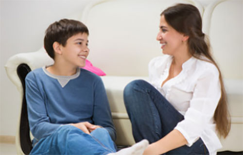 Мама весело общается с сыном, сидя на полу возле дивана