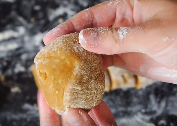 Женщина разрезала тесто на шесть частей. Одну держит в руке