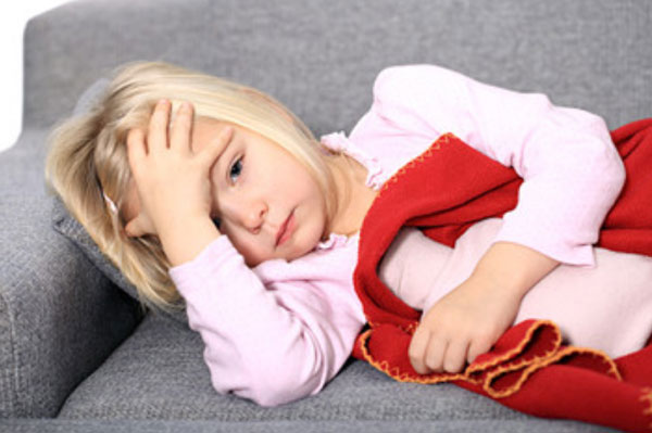 Девочка лежит на диване, держится за голову