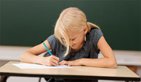 Девочка сидит за партой и увлеченно пишет в тетради