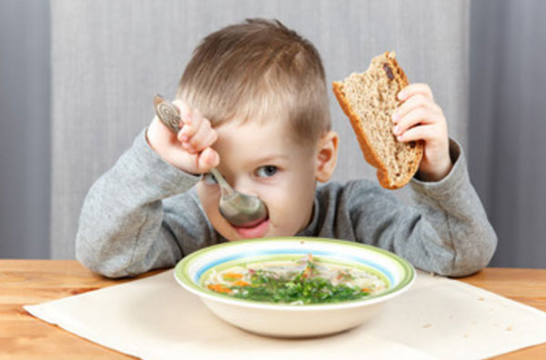 Мальчик ест суп с хлебом