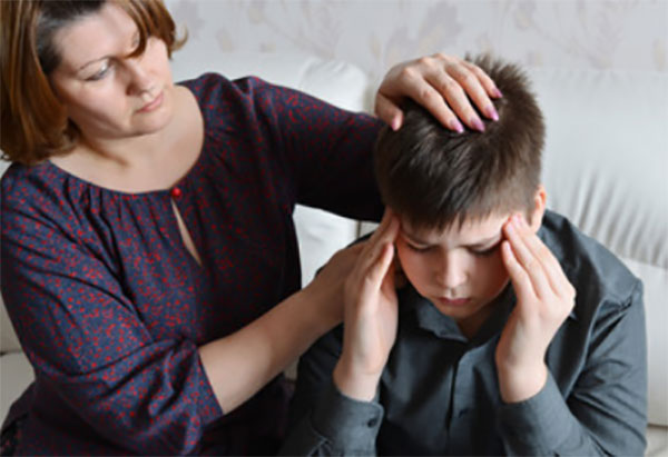 Мальчик держится за голову. Рядом сидит мама