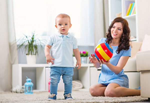 Мама держит мяч, рядом стоит ее маленький сын