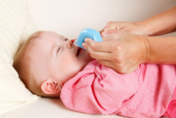 Мама спринцовкой очищает носик малыша