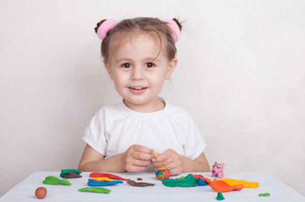 Маленькая девочка сидит за столом, собирается лепить