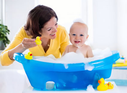 Маленький ребенок принимает ванну, рядом сидит мама