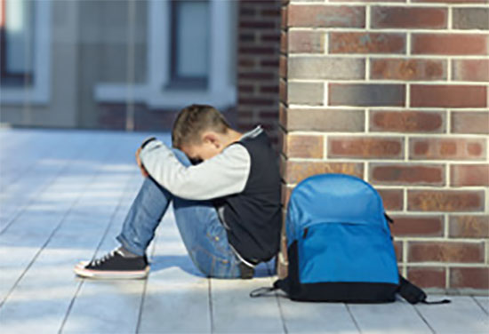 Мальчик сидит возле стены, рядом лежит рюкзак