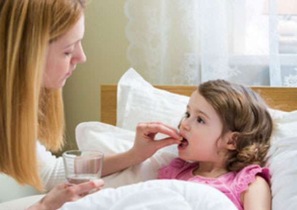 Мама дает таблетку дочери, которая лежит в постели
