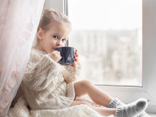 Девочка сидит на окне с чашкой в руках. Она что-то пьет