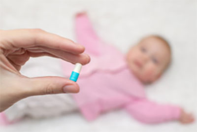 Рука женщины с капсулой. На заднем плане грудничок