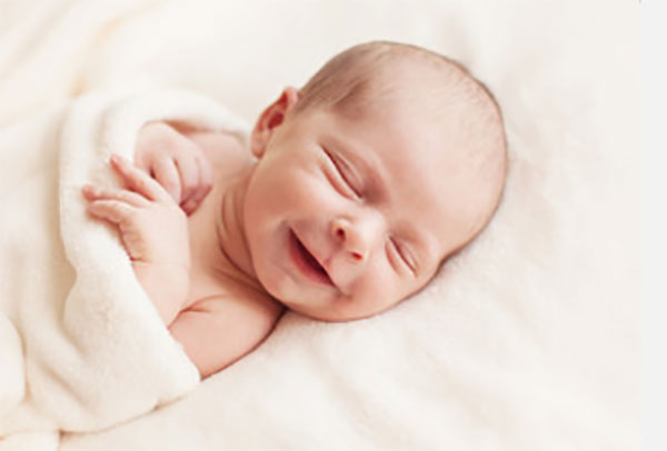 Грудной ребенок спит и улыбается, одна ручка сжата в кулачке