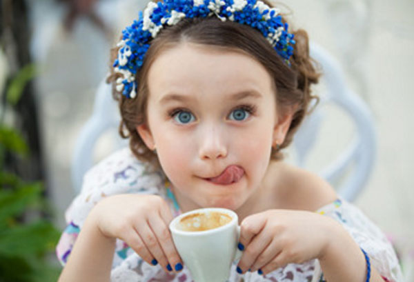 Девочка держит в руках пустую чашку от кофе и облизывается