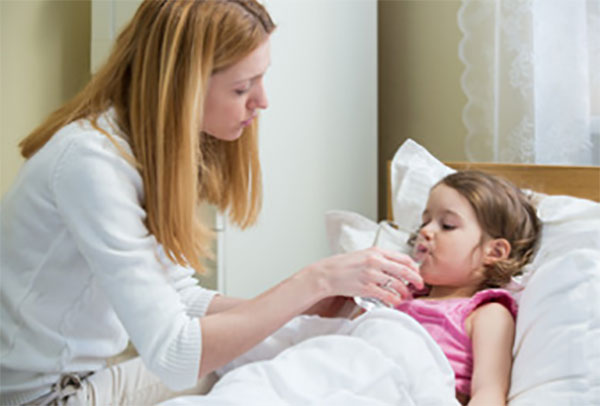 Мама дает девочке, лежащей в постели, лекарство
