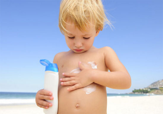 Мальчик наносит крем от загара на свое тело