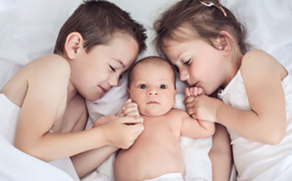 На кровати трое детей. Посередине самый маленький - грудничок