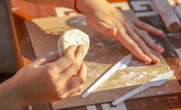 Досточка, на ней лежат два ножичка. Ребенок держит тесто в руке