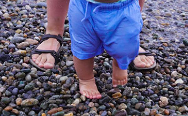 Родитель водит маленького ребенка босиком по гальке