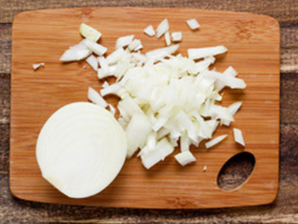 Покрошенный лук на досточке, рядом целая половинка