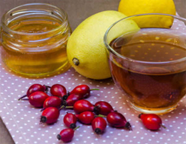 Напиток в стакане, рядом лежит мед, лимон и шиповник