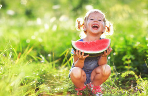 Смеющаяся девочка с куском арбуза сидит в траве