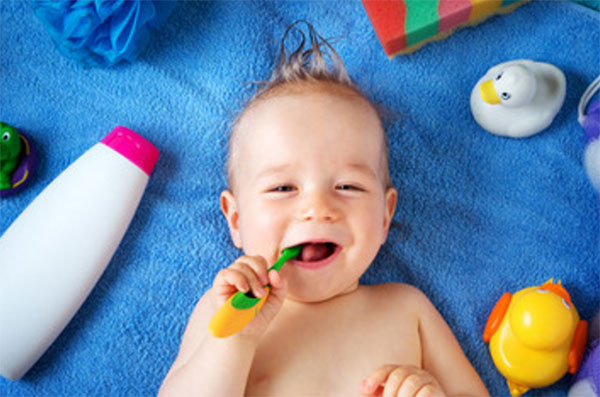 Лежит ребенок, во рту держит зубную щетку. Вокруг предметы для купания