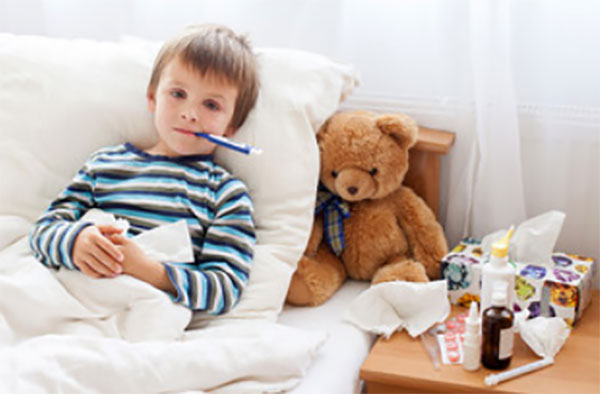 Больной мальчик в постели с градусником во рту