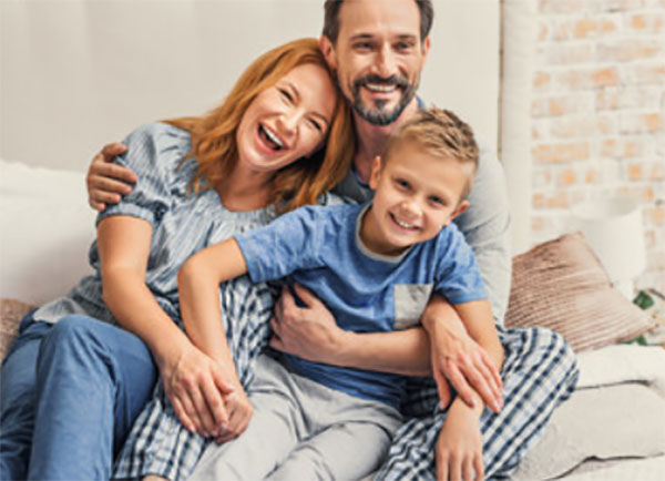 Папа, мама и сын обнимают друг друга, сидя на диване