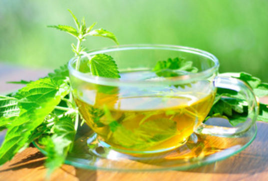 Чашка с настоем крапивы, рядом лежат листочки этого растения