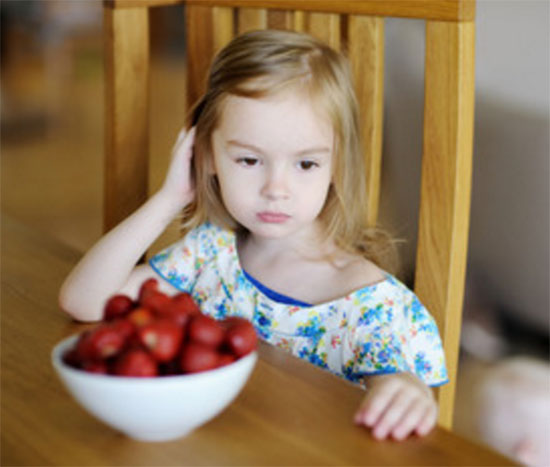 Сидит грустная девочка, перед ней глубокая тарелка с клубникой.